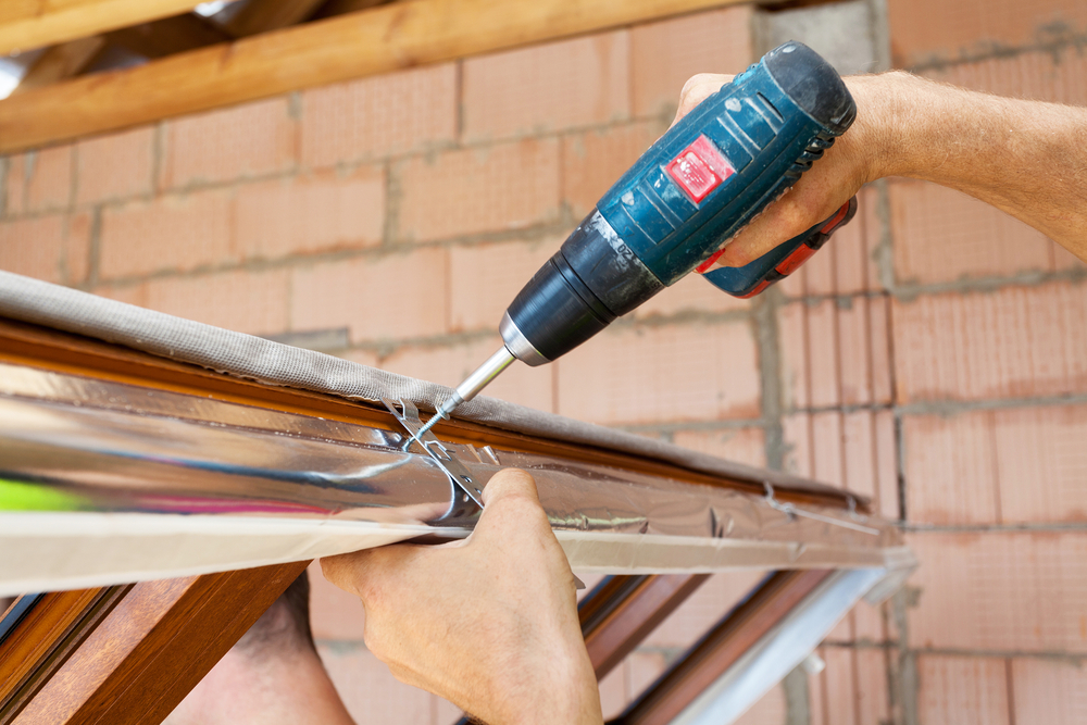 Installer drilling screw into window frame